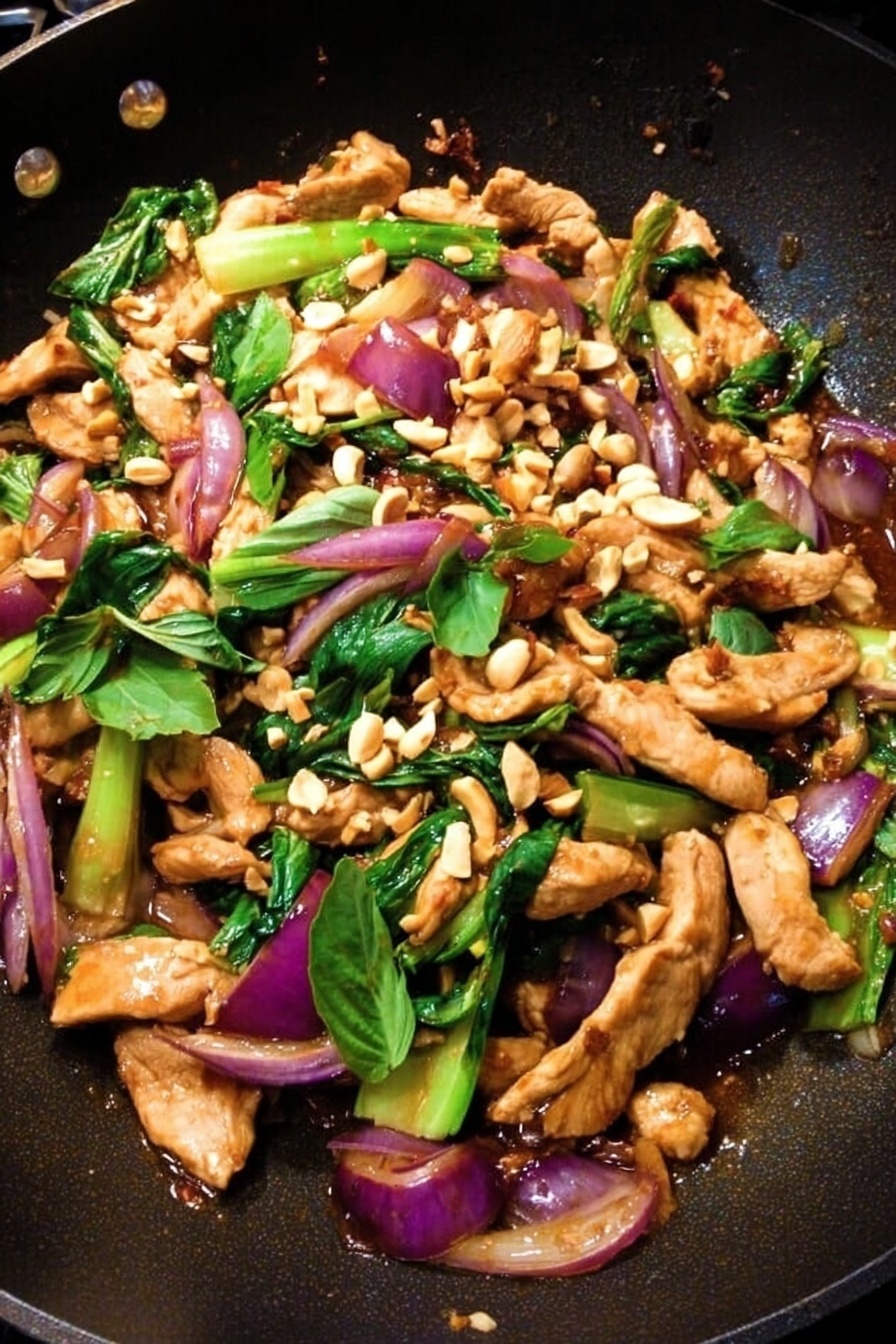 A black wok filled with strips of light brown cooked chicken on top, layered with bright green bok choy pieces and vibrant purple-red cooked onions. Scattered over everything are small beige chopped peanuts and fresh green basil leaves. The ingredients mix with a slight shine from the sauce, giving the dish a fresh and colorful look. photo taken with an iphone --ar 2:3 --v 7