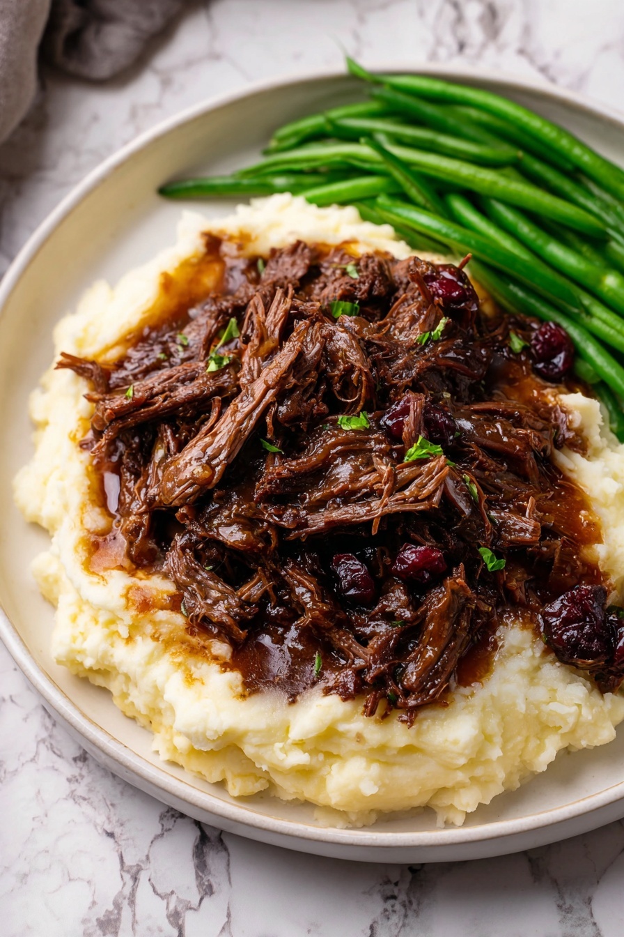 A white plate holds a dish with three layers: the bottom layer is smooth, creamy mashed potatoes in pale white, spread evenly across the plate; the middle layer is made up of dark brown shredded beef with visible tender texture, covered with a glossy rich sauce and small bits of onions and cranberries; the third layer is green beans, bright and fresh, positioned to the side of the beef and potatoes. The plate sits on a surface with a white marbled texture. Photo taken with an iphone --ar 2:3 --v 7