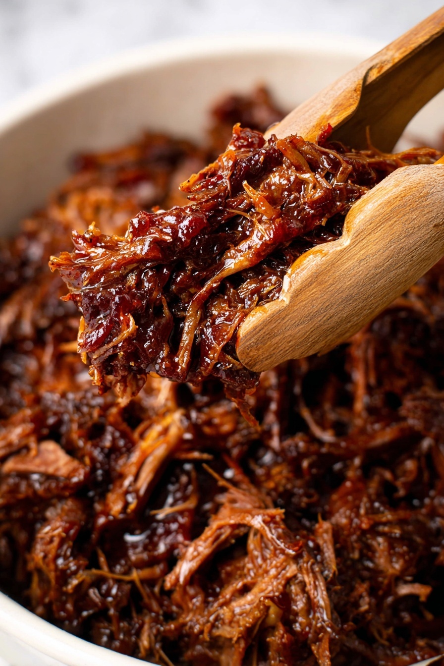 A close-up view shows shredded dark brown meat with a glossy, moist texture held by wooden tongs above a white bowl filled with more of the same shredded meat, which has visible strands and a rich, saucy coating, sitting on a white marbled surface. photo taken with an iphone --ar 2:3 --v 7