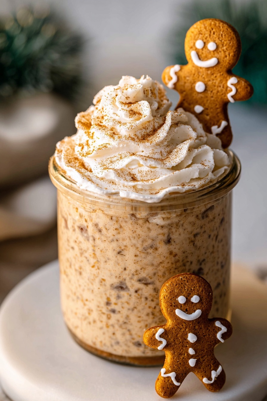 A clear glass jar filled with a thick, creamy mixture of light brown color with visible darker brown specks and small grains spread throughout. On top of the jar is a swirl of white whipped cream sprinkled with light brown powder. A small gingerbread man cookie with white icing details stands partially dipped into the mixture at the edge of the jar. The jar sits on a white round plate on a white marbled surface. The background is softly blurred with hints of green and white shapes. Photo taken with an iphone --ar 2:3 --v 7
