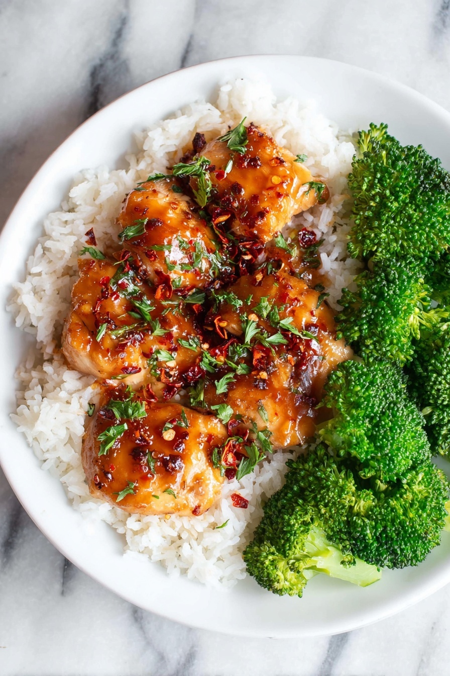 A white plate holds a base layer of fluffy white rice, topped with several pieces of glossy, golden-brown chicken glazed in a shiny sauce with red chili flakes and chopped green herbs scattered on top. On the right side of the plate, bright green, steamed broccoli florets add a fresh contrast in color and texture, all placed on a white marbled surface. photo taken with an iphone --ar 2:3 --v 7