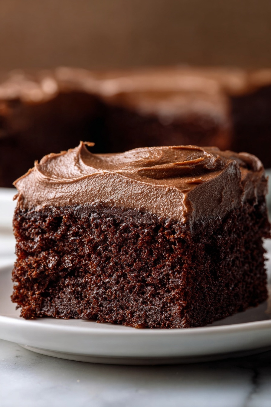 A close-up view of a single square piece of chocolate cake on a white plate, showing two layers: the bottom layer is a rich, moist dark brown chocolate cake with a soft and crumbly texture, and the top layer is a thick, smooth, and creamy chocolate frosting with a slightly glossy surface that spreads evenly over the cake with gentle swirls. The background is softly blurred with warm brown tones, and the scene is set on a white marbled surface. Photo taken with an iphone --ar 2:3 --v 7