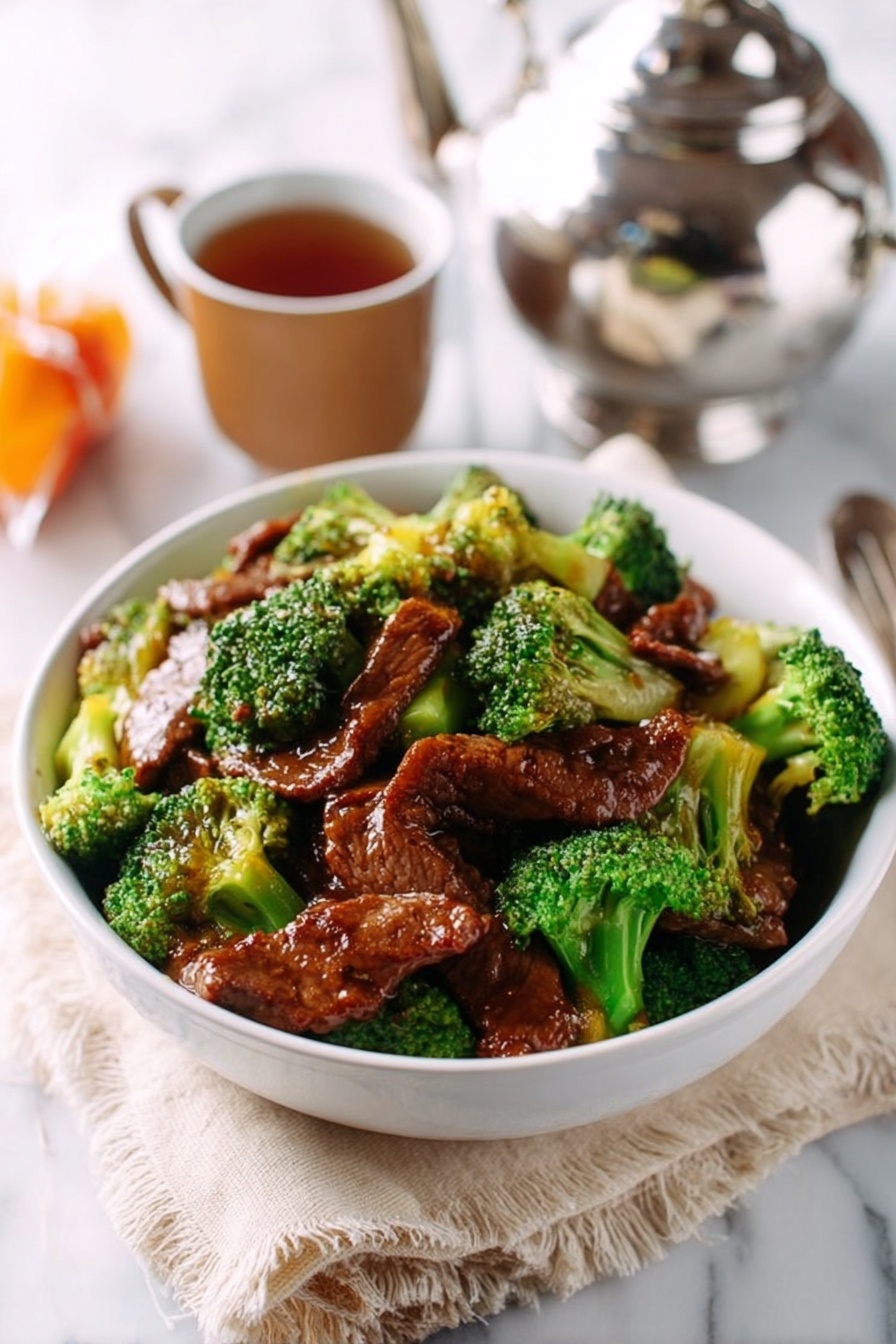 A white bowl filled with stir-fried beef slices and bright green broccoli florets. The beef is coated with a shiny brown sauce that makes it look tender and juicy, sitting on top and mixed with the vibrant broccoli. The bowl rests on a light beige cloth with rough edges, placed on a white marbled surface. In the background, there is a shiny silver teapot, a small brown cup with tea, and a small wrapped orange item, all slightly out of focus. photo taken with an iphone --ar 2:3 --v 7