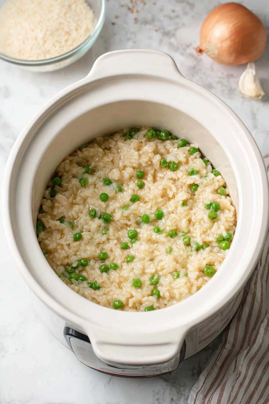 The image shows a white bowl filled with creamy risotto mixed with bright green peas scattered throughout. The risotto has a soft and creamy texture with small grains of rice visible, seasoned lightly with specks of black pepper on top. In the background, there is a clear glass bowl with uncooked rice grains, a garlic bulb, and a white rice cooker with orange and red indicator lights. A red shallot and some cheese shavings can also be seen on the white marbled surface beneath the bowl and surrounding items. photo taken with an iphone --ar 2:3 --v 7