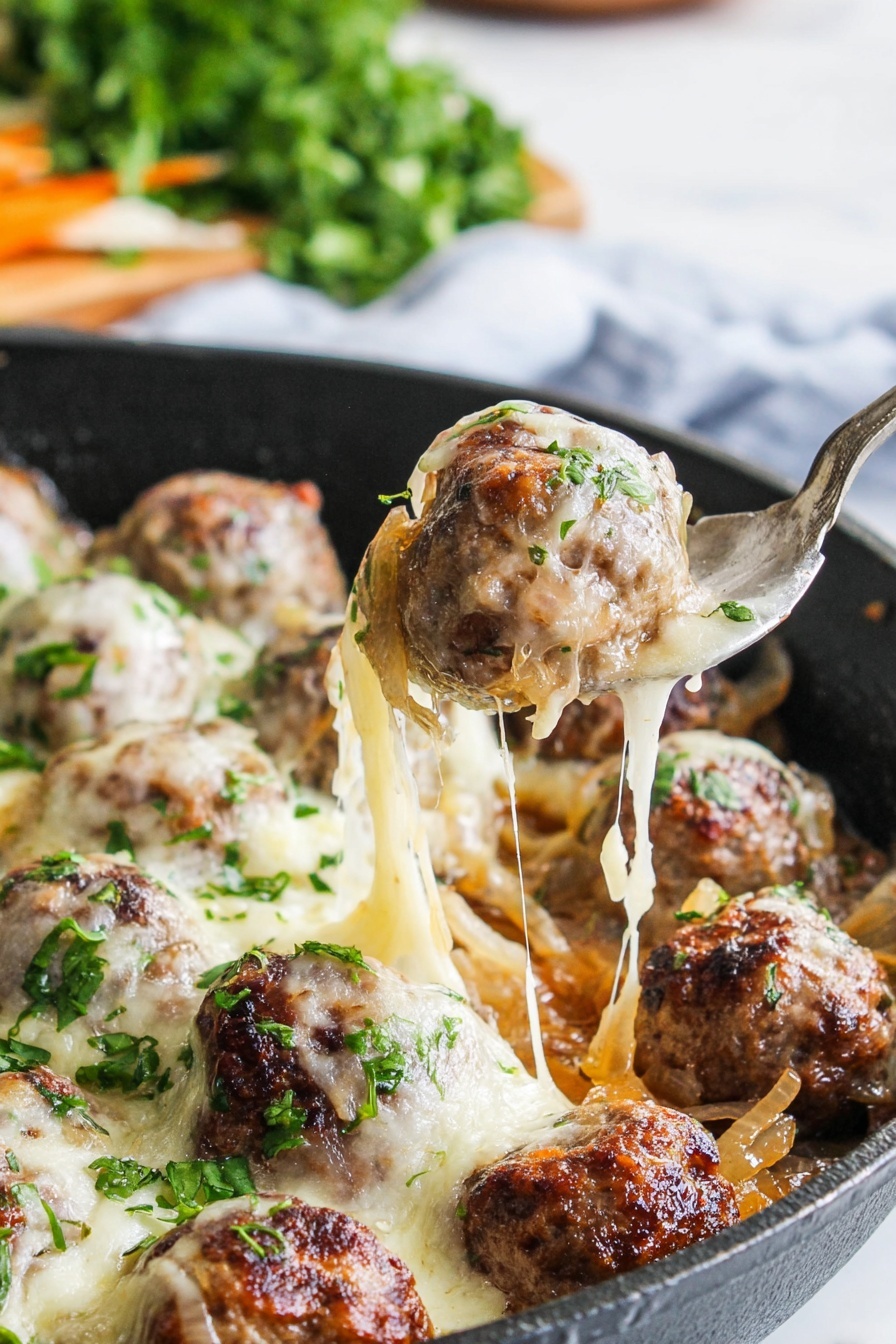 The image shows a close-up of a black pan filled with multiple meatballs covered in melted, stretchy cheese. The meatballs are brown with a slightly seared texture and are nestled among soft, light golden cooked onions. Fresh green chopped herbs are sprinkled on top, adding a pop of color. A metal spoon is lifting one meatball, pulling a long strand of melted cheese away from the pan. The background is blurred with green herbs on a white marbled surface. photo taken with an iphone --ar 2:3 --v 7