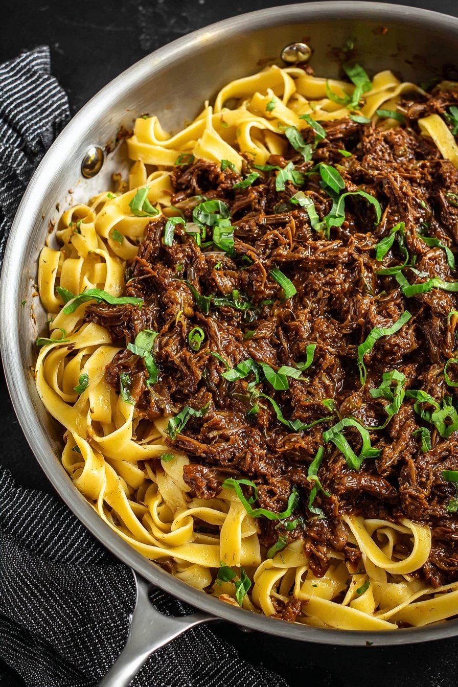 A shallow white bowl is filled with wide, flat pasta noodles mixed with dark brown shredded meat, evenly distributed throughout the dish. The pasta is coated in a rich sauce, with small bits of green herbs scattered on top for color. The noodles have a slightly glossy texture, twisting and turning around the meat. There is a silver fork stuck into the noodles on the right side of the bowl. In the background on the upper left, a small beige bowl with chunks of pale yellow cheese sits on a white marbled surface. The overall scene is simple and rustic, with the focus on the hearty pasta dish. photo taken with an iphone --ar 2:3 --v 7