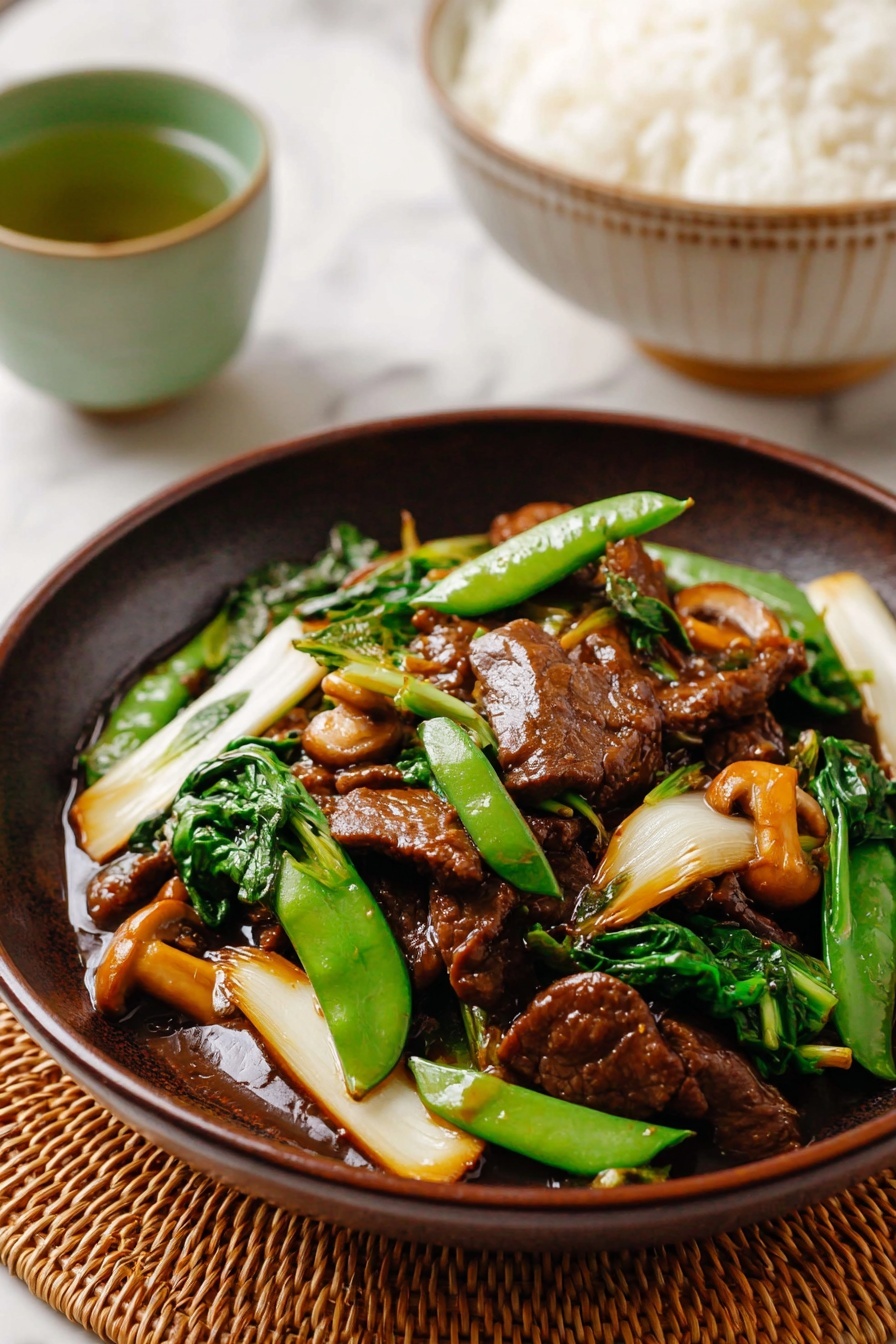 A dark brown bowl holds a stir-fry dish with three main layers: the bottom layer has a glossy, thick brown sauce coating everything; the middle layer contains shiny, cooked green sugar snap peas, dark green leafy vegetables, and pale yellow bok choy with patches of bright white and light green stems; the top layer features browned, tender-looking slices of meat and small brown mushrooms, evenly mixed and covered with sauce. The bowl sits on a light tan bamboo mat over a white marbled surface. In the background, there is a white bowl with a blue pattern filled with plain white rice and a small cup of green tea. Wooden chopsticks rest on the bamboo mat next to the bowl. Photo taken with an iphone --ar 2:3 --v 7