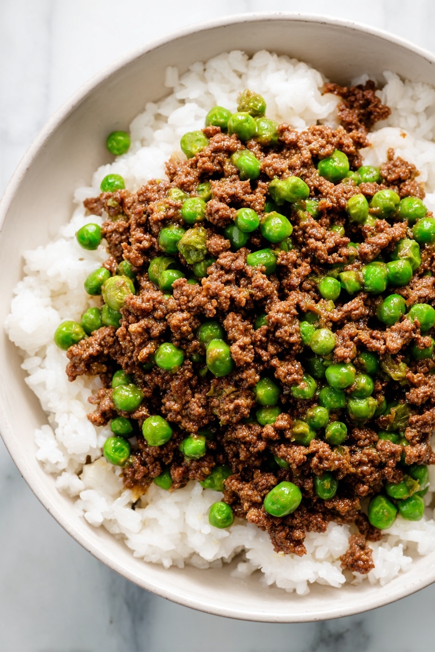 This image shows a white bowl filled with two layers of food. The bottom layer is white rice with soft, fluffy grains spread evenly across the bowl. On top is a mix of small brown cooked ground meat pieces and bright green peas scattered throughout. The colors contrast well with the bright white rice, and the texture of the meat looks crumbly while the peas look smooth and round. The bowl sits on a white marbled surface. photo taken with an iphone --ar 2:3 --v 7