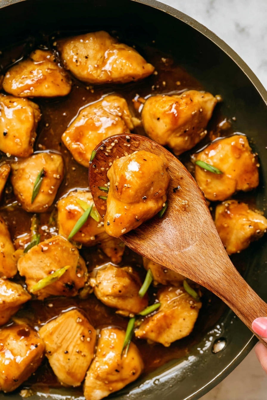 The image shows several pieces of golden-brown chicken coated in a shiny, thick sauce with specks of black pepper, placed in a sauté pan. The chicken pieces are plump and slightly browned on the edges, with some green onion slices scattered on top adding a pop of color. A wooden spoon held by a woman's hand is lifting two pieces of chicken from the pan, showing the glossy sauce pooling around them. The background visible beneath the pan is a white marbled texture, giving a clean and bright look to the scene. photo taken with an iphone --ar 2:3 --v 7