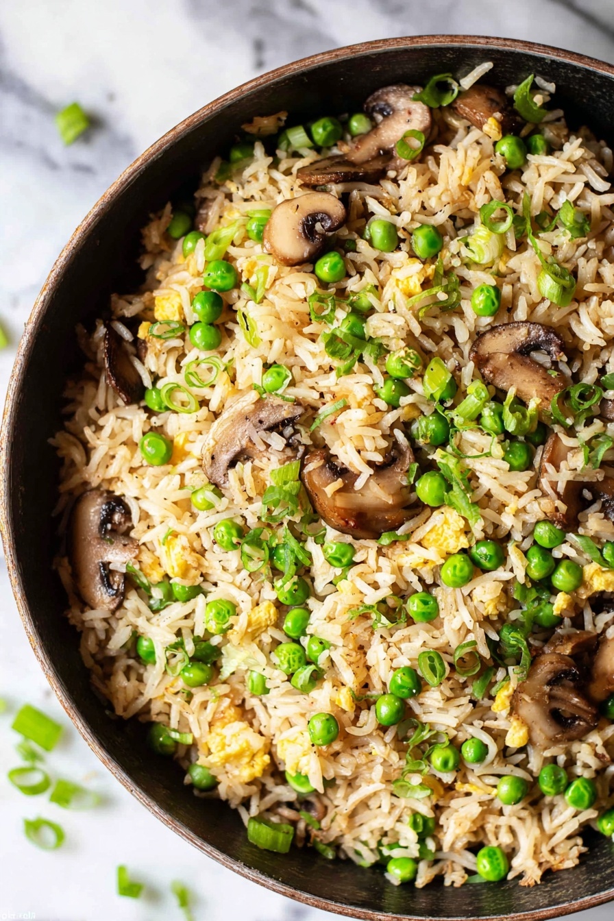 A close-up view of a black pan filled with fried rice that has three main layers: the bottom layer is light brown cooked rice with a fluffy texture, the middle layer has bright green peas and chopped green onions, and the top layer includes sliced brown mushrooms and small pieces of cooked egg scattered throughout. The pan sits on a white marbled surface with some green onion pieces around the pan edge. The rice looks mixed well with all ingredients evenly spread. photo taken with an iphone --ar 2:3 --v 7