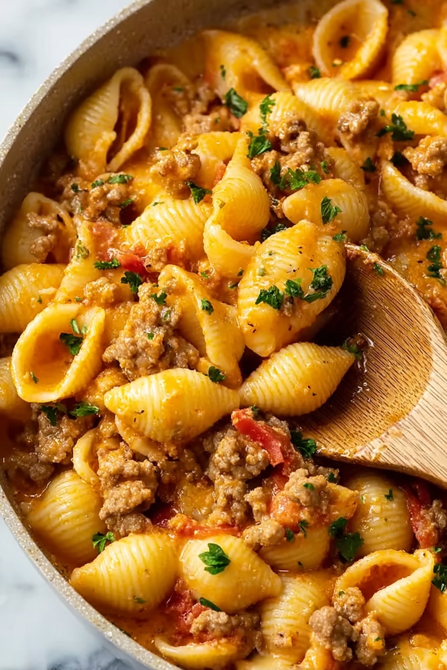 The image shows a close-up view of a pasta dish with shell-shaped noodles mixed with a creamy orange sauce. The sauce includes small pieces of cooked ground meat that are light brown, along with bits of red tomatoes and green parsley sprinkled throughout. The pasta shells are coated well with the sauce, which looks smooth and rich. A wooden spoon is partially visible on the right side, buried in the pasta, showing the texture of the noodles and sauce. The background surface has a white marbled texture. photo taken with an iphone --ar 2:3 --v 7