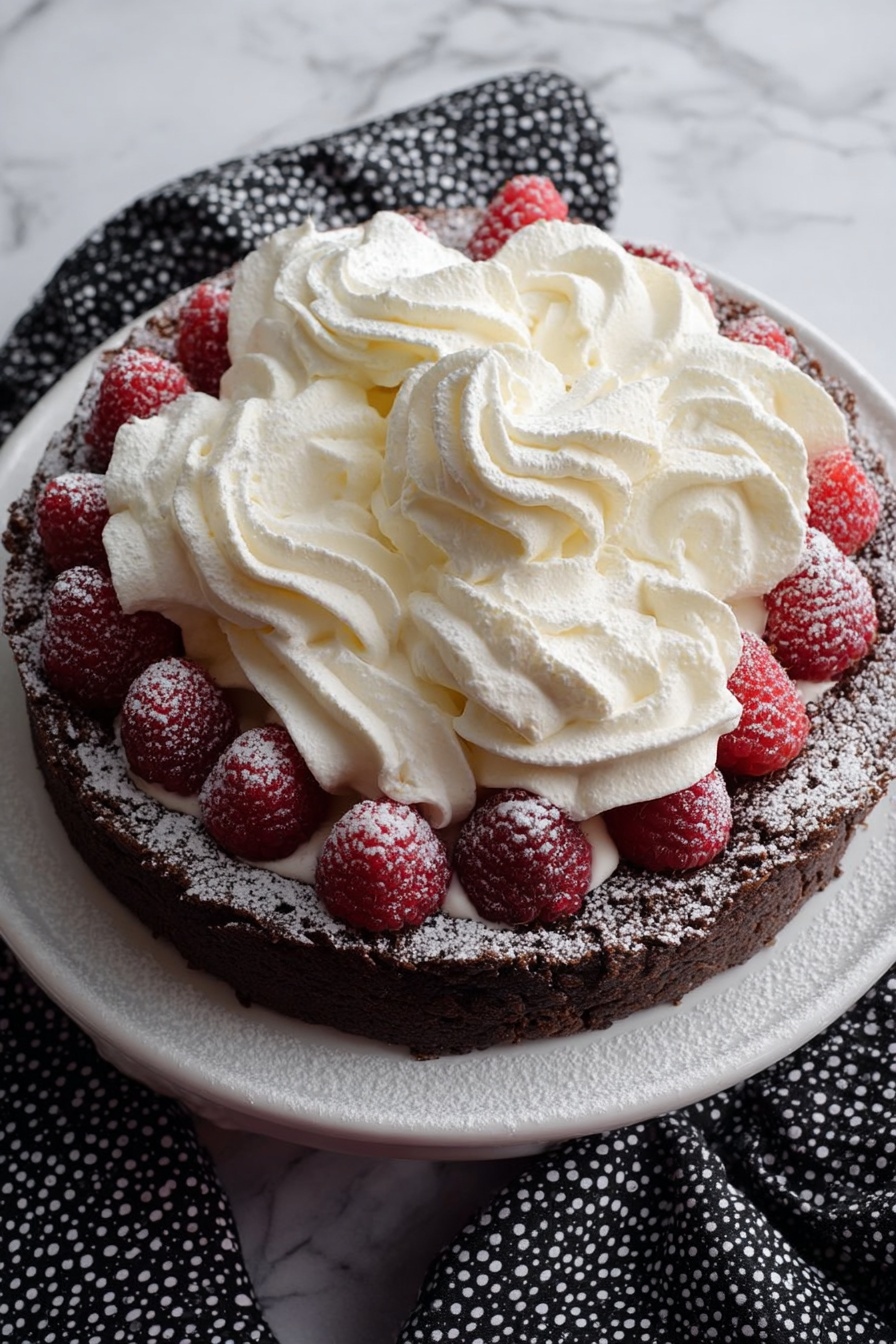 A round dessert with a cracked dark brown crust base dusted lightly with powdered sugar. On top of the crust, there is a thick layer of white whipped cream piped in tight swirls, covering the center fully. Around the edges, bright red raspberries dusted with powdered sugar line the dessert, placed on a white plate surrounded by a dark cloth with small white patterns, all set on a white marbled surface. photo taken with an iphone --ar 2:3 --v 7