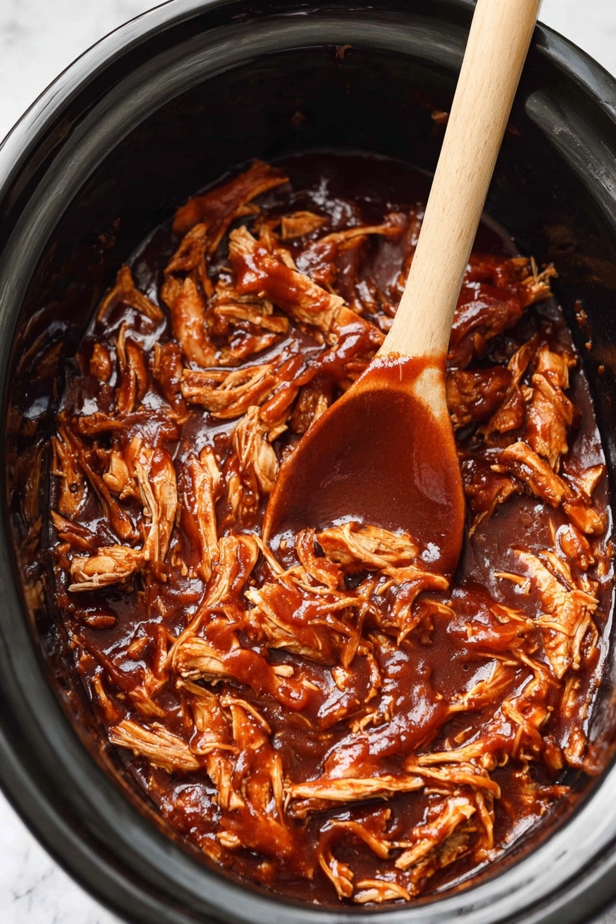 This image shows a black slow cooker filled with shredded chicken covered in thick, glossy dark brown barbecue sauce. The chicken pieces vary in size and texture, some larger and chunky, others smaller and stringy, spread evenly throughout the thick sauce. A light wooden spoon with a smooth texture lies on top of the chicken, partially submerged with the tip covered in sauce. The background around the pot is a white marbled texture. photo taken with an iphone --ar 2:3 --v 7